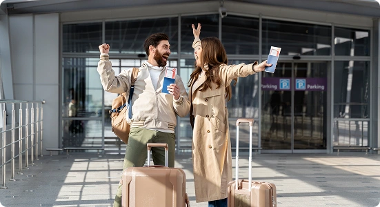 Two travelers celebrate outside a modern terminal with rolling suitcases, high-fiving as they hold tickets and phones.